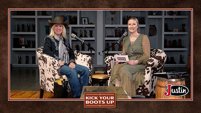 Two women looking at the camera, smiling, and sitting in chairs having a conversation.